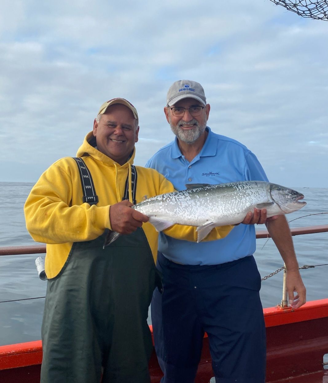 Two men standing on a boat holding a large fish