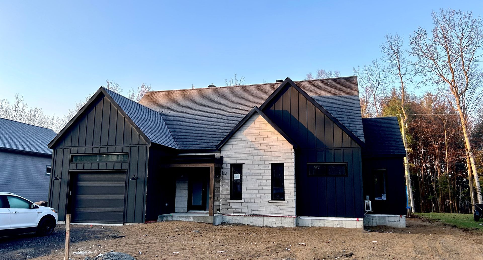 Une voiture blanche est garée devant une maison en construction.