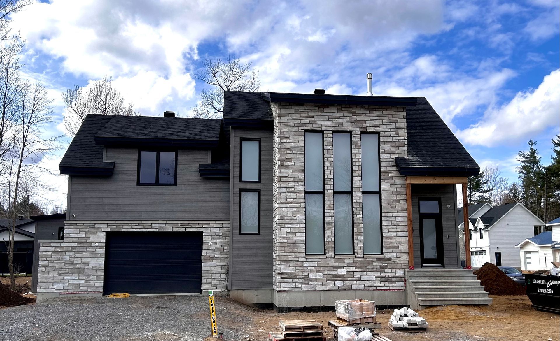 Une grande maison avec une porte de garage noire est en construction.