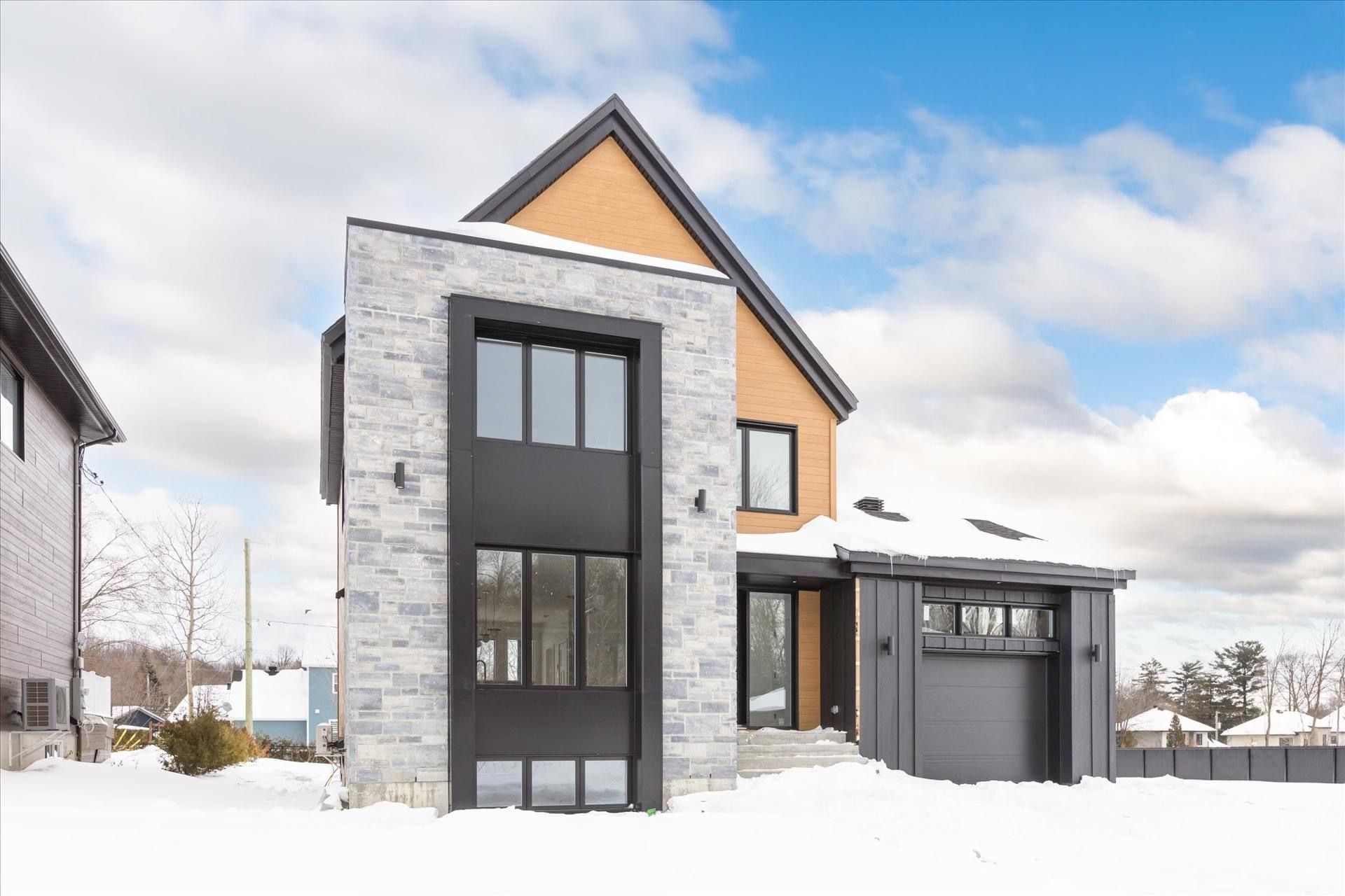 Une maison moderne avec un garage et beaucoup de fenêtres est couverte de neige.