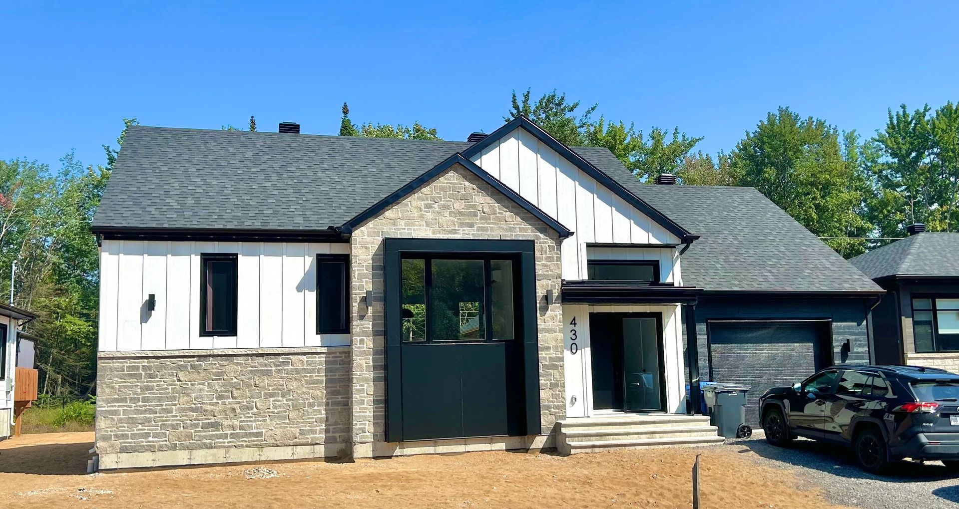 Une maison noire et blanche avec une voiture garée devant.