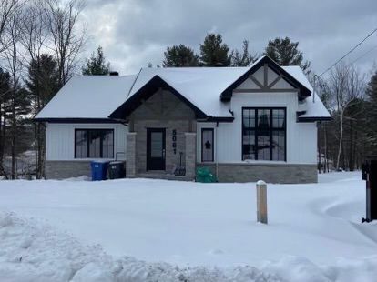 Une maison blanche au toit noir est recouverte de neige.