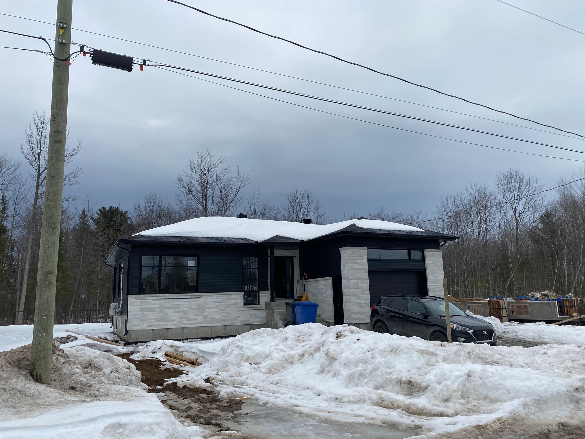 Une voiture noire est garée devant une maison couverte de neige
