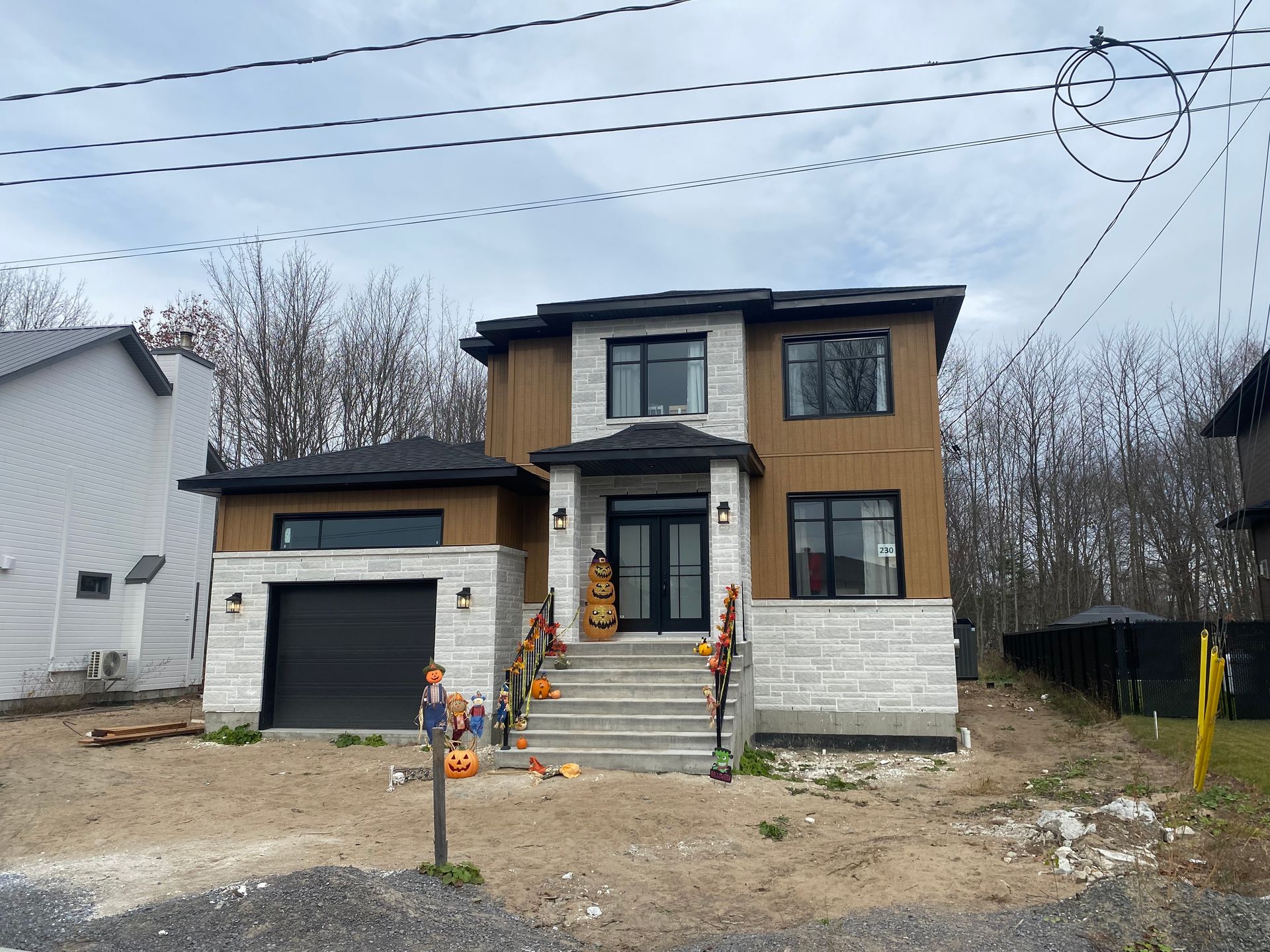 Maison à deux étages avec revêtement en pierre et bois, fenêtres et porte noires, et un escalier menant à la porte d'entrée. Citrouilles et décorations d'Halloween ornent les marches.