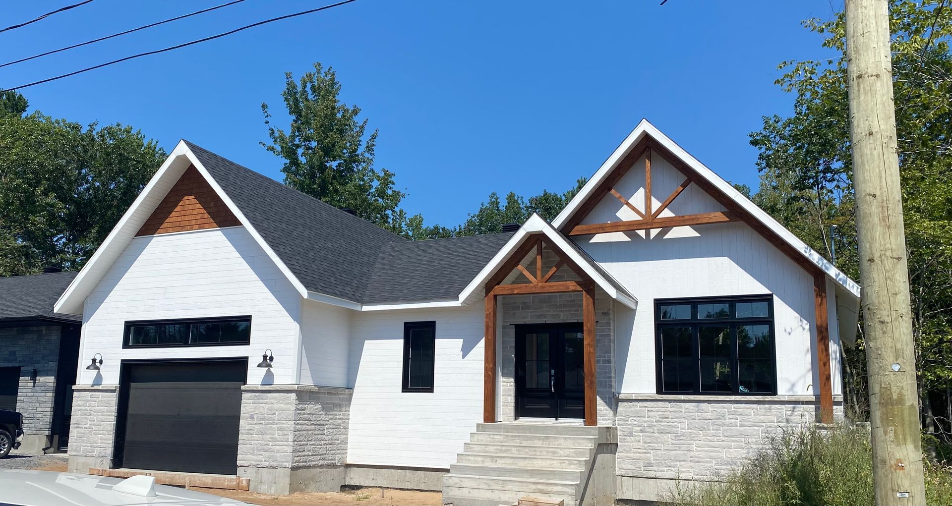 Une maison blanche au toit noir est en construction.