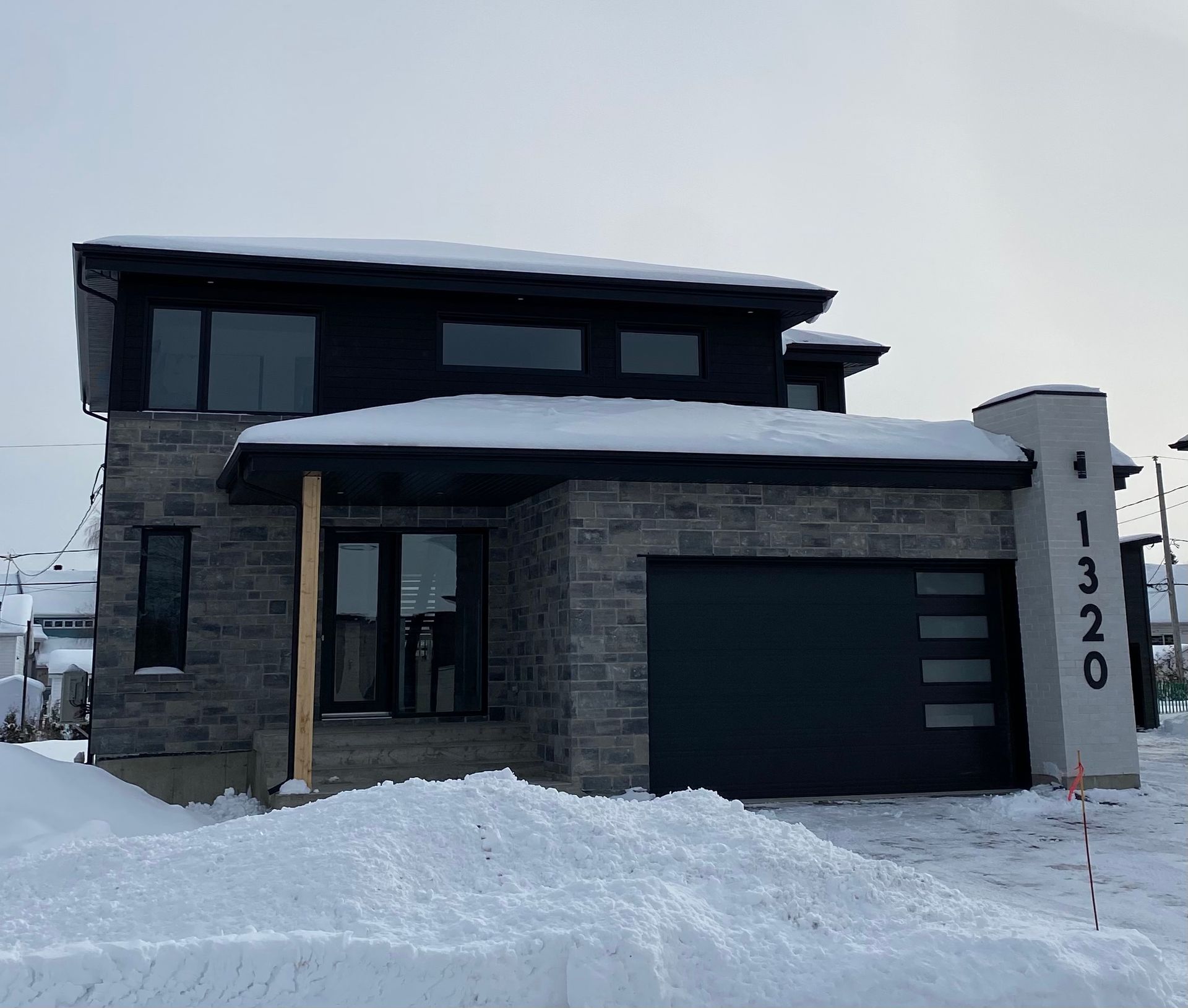 Une maison avec une porte de garage noire est couverte de neige.