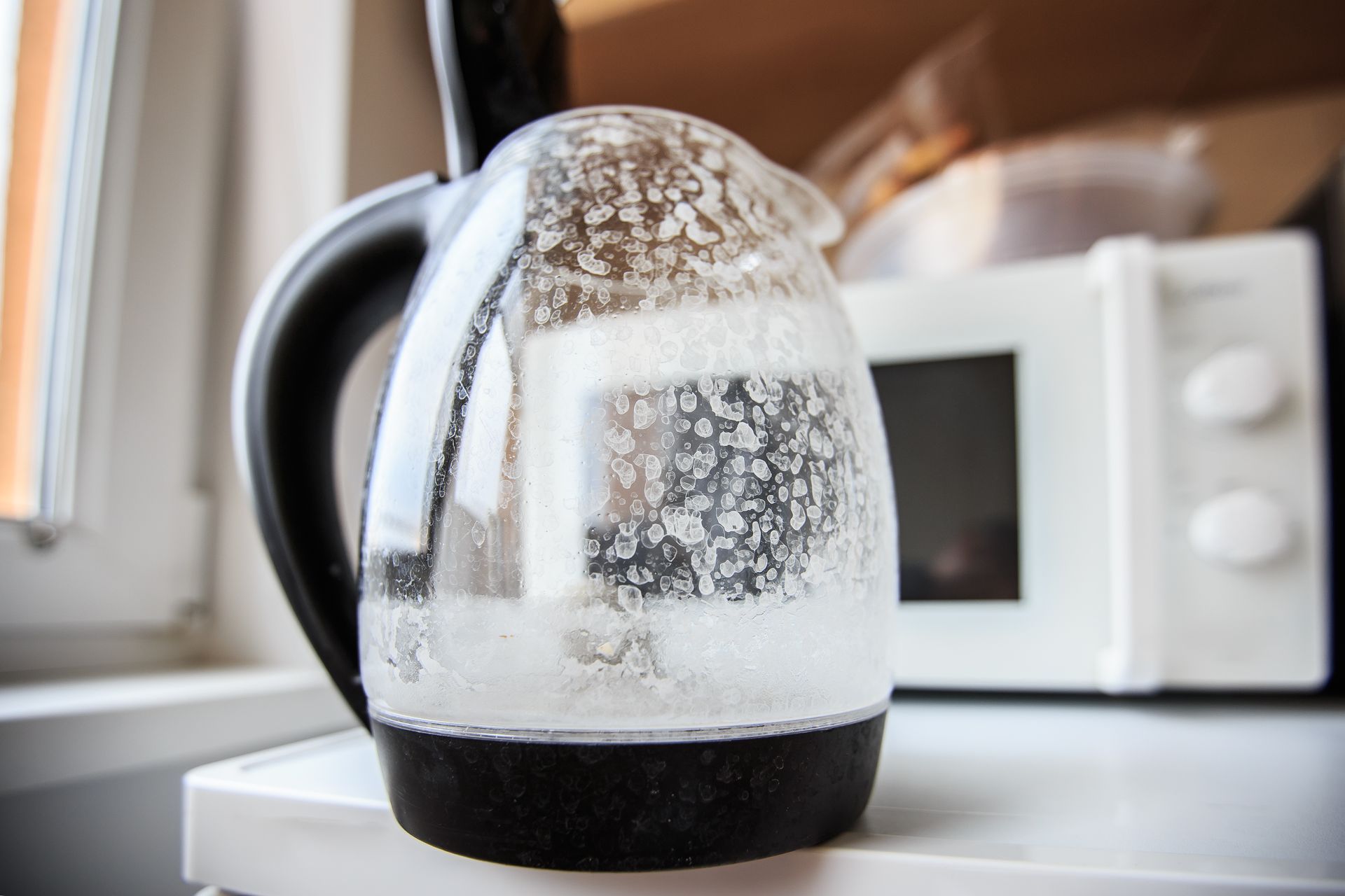 A glass kettle is sitting on a counter next to a microwave.