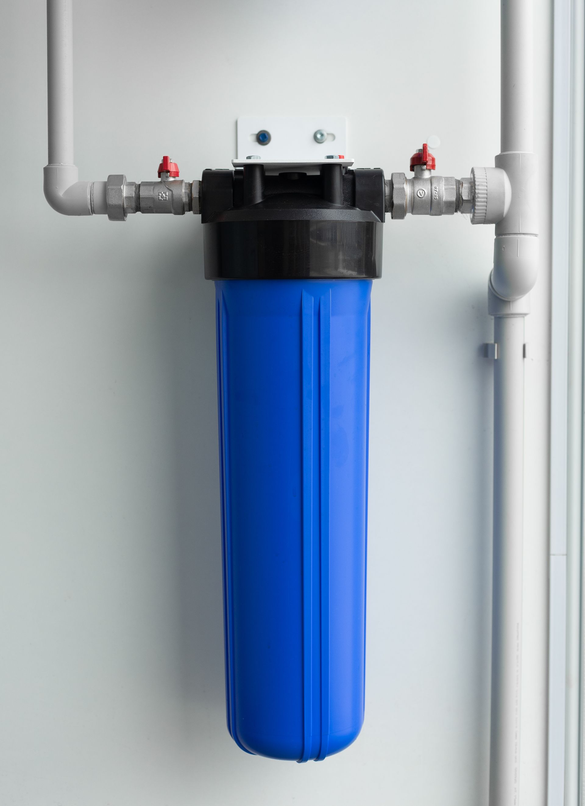 A blue water filter is attached to a pipe on a wall.