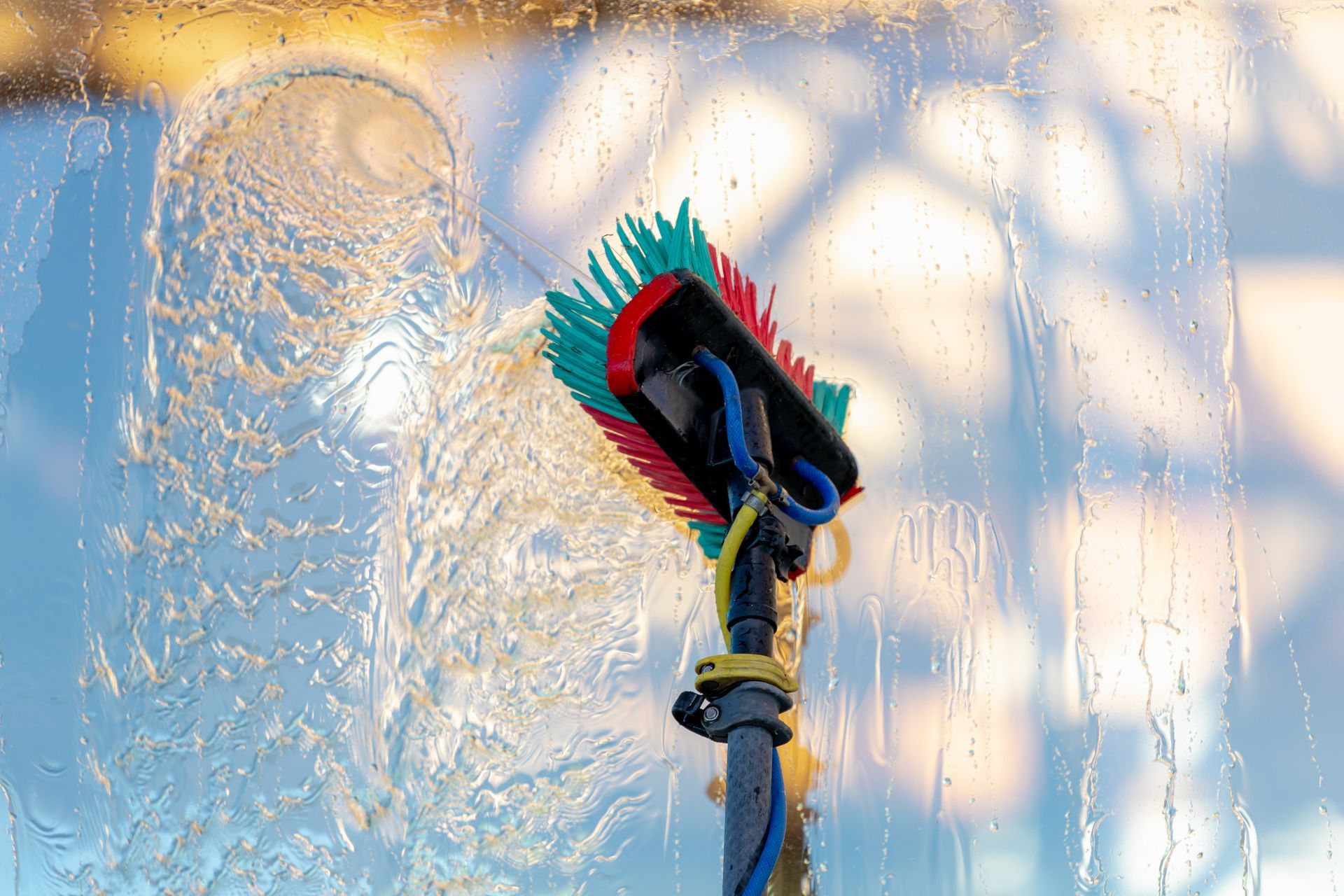 A brush is cleaning a window with water coming out of it.
