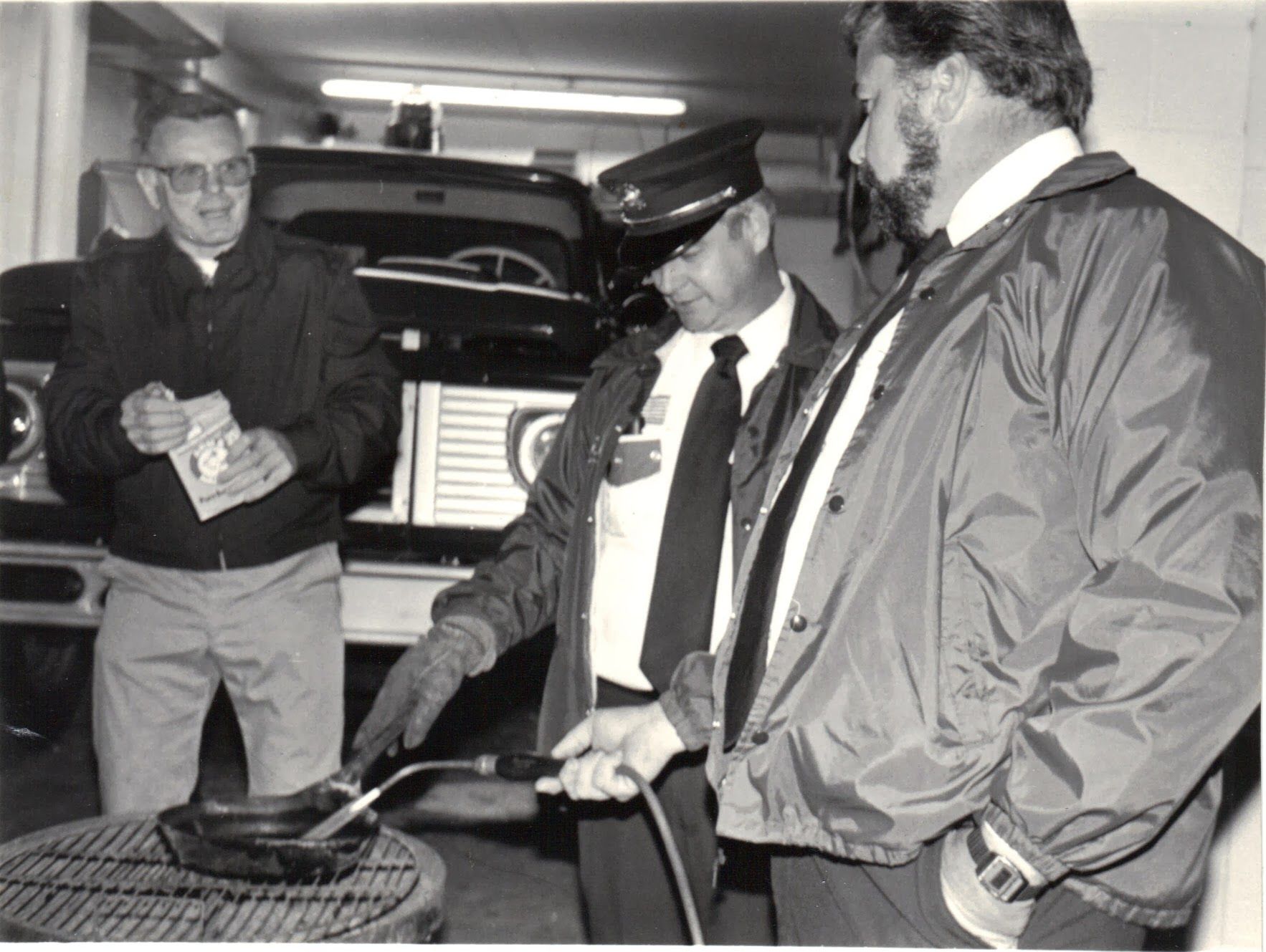 A black and white photo of three men standing around a grill