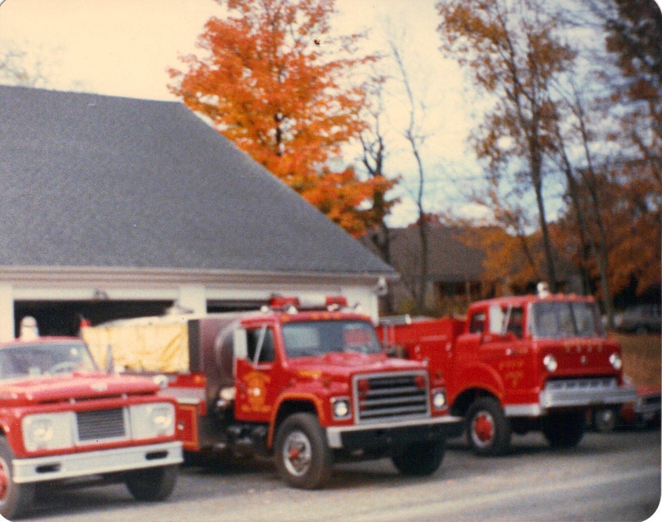 Three red fire trucks are parked in front of a garage