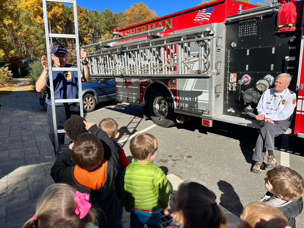 A group of children are sitting in front of a fire truck.