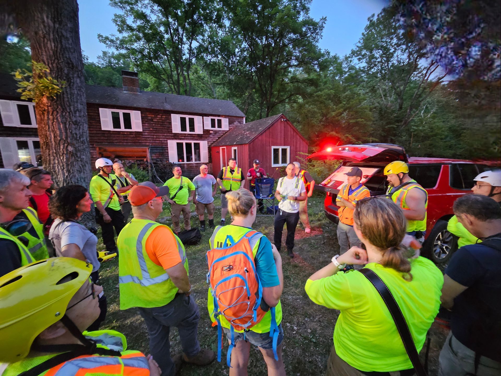A group of people are standing in a circle in front of a red house.