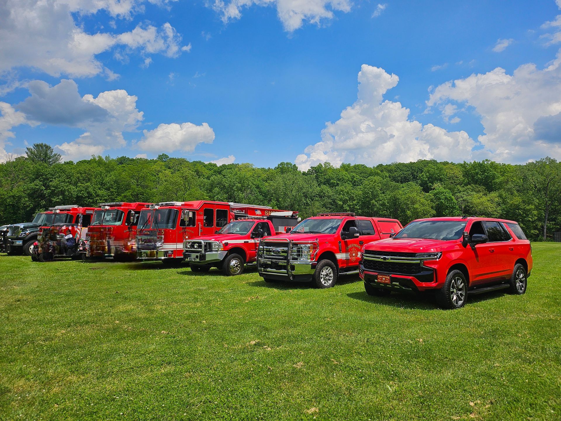 A row of red fire trucks are parked in a grassy field.
