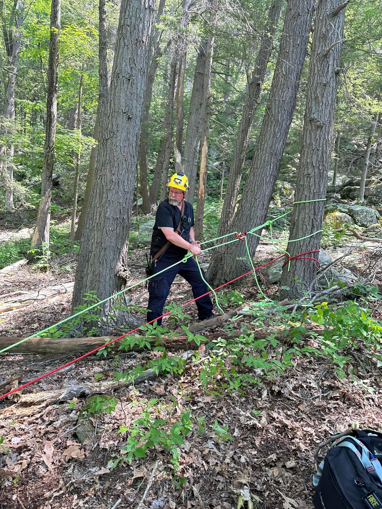 A man is standing in the woods holding a rope.