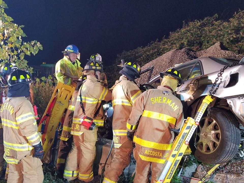 A group of firefighters are standing around a wrecked car.