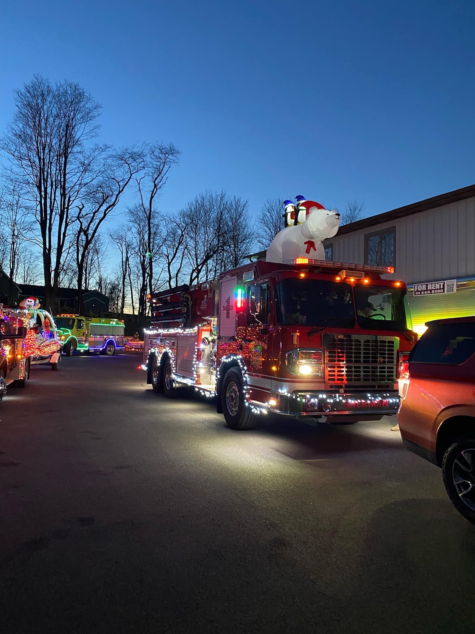 A fire truck decorated for christmas is driving down a street at night.