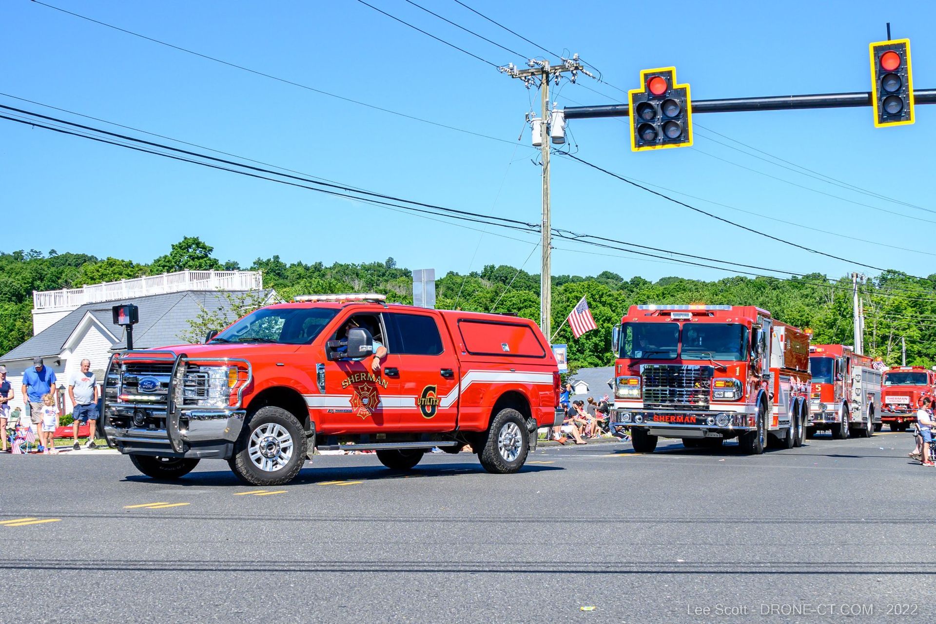 A row of fire trucks are driving down a street in a parade.