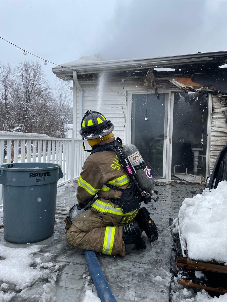 A fireman is kneeling down in front of a house with a hose.