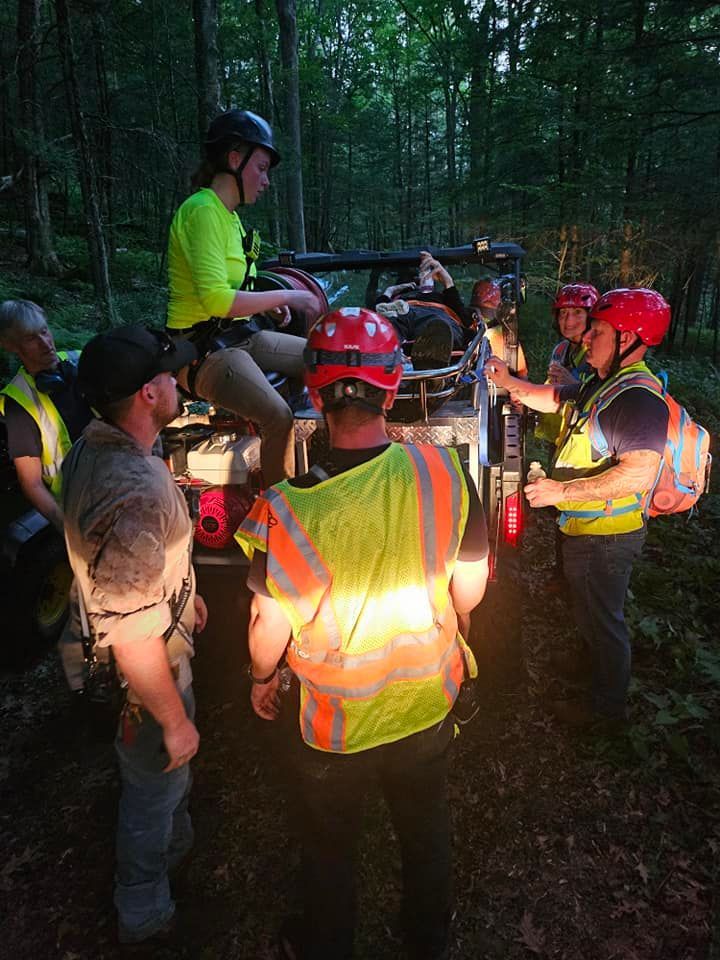 A group of people are standing around a vehicle in the woods.