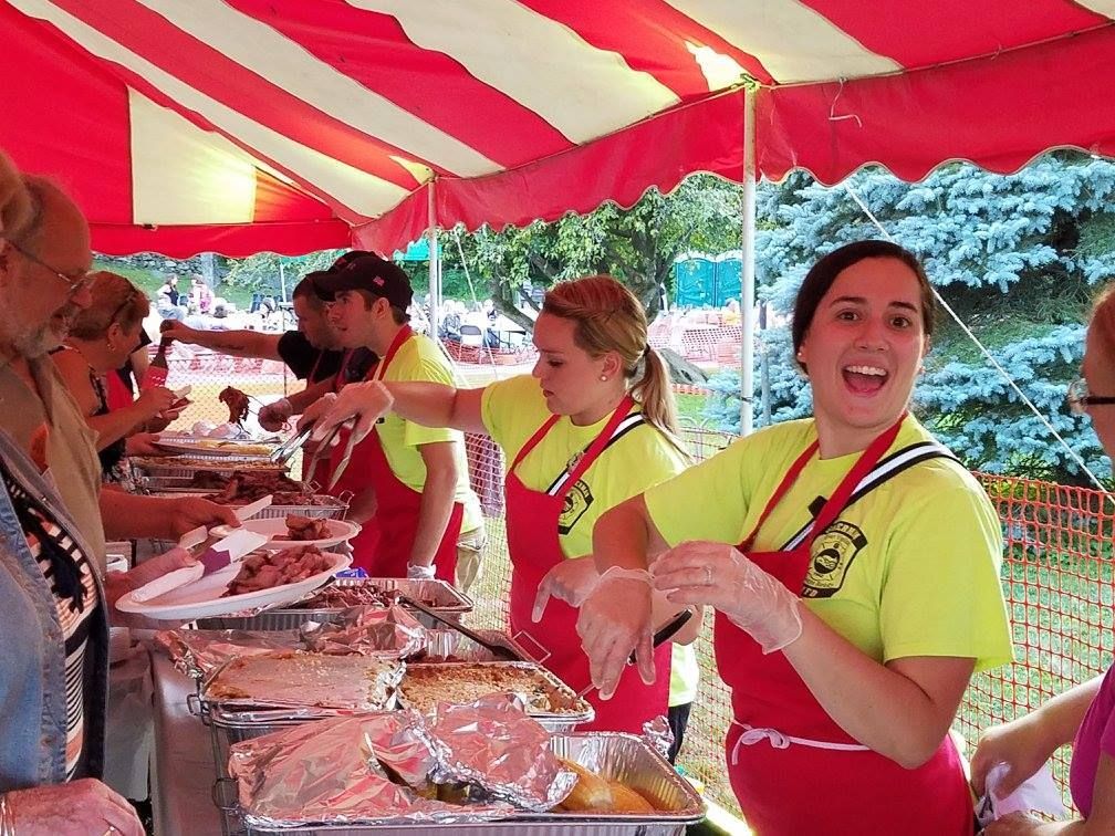 A group of people are serving food under a red and white tent.