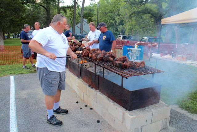 A man is cooking meat on a grill in a parking lot