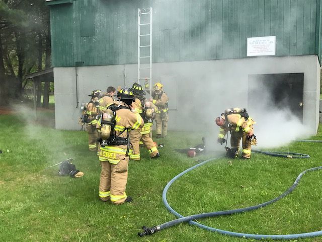 A group of firefighters are standing in front of a building with smoke coming out of it.