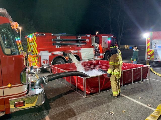 A fire truck is pumping water into a red tank.