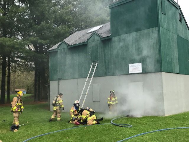 A group of firefighters are standing in front of a green building with smoke coming out of it.