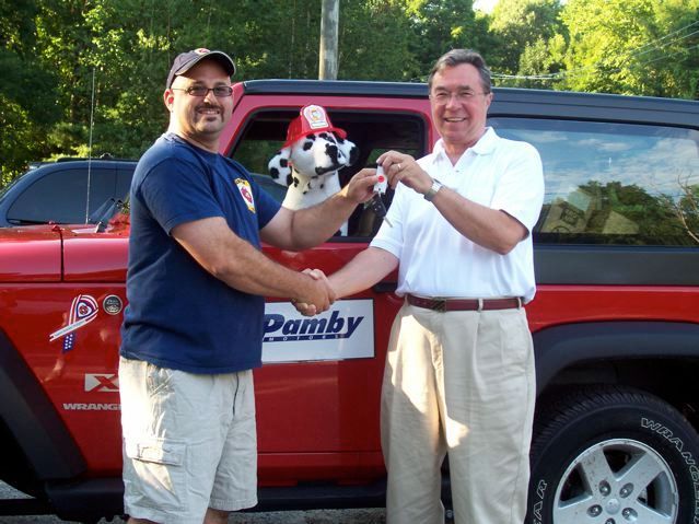 Two men shaking hands in front of a red pamby jeep