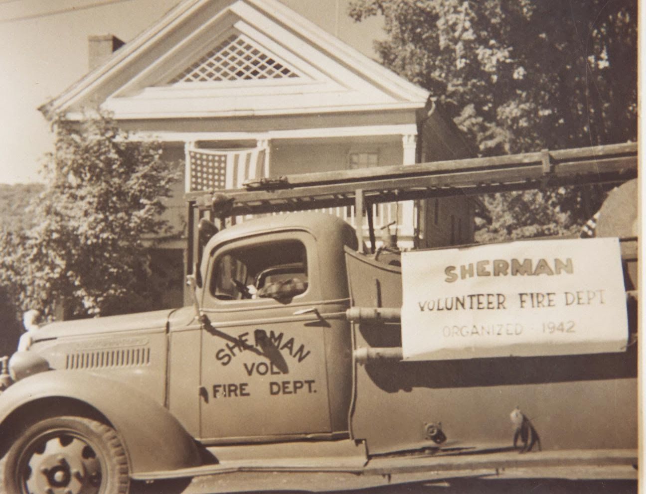 A sherman volunteer fire dept truck is parked in front of a house