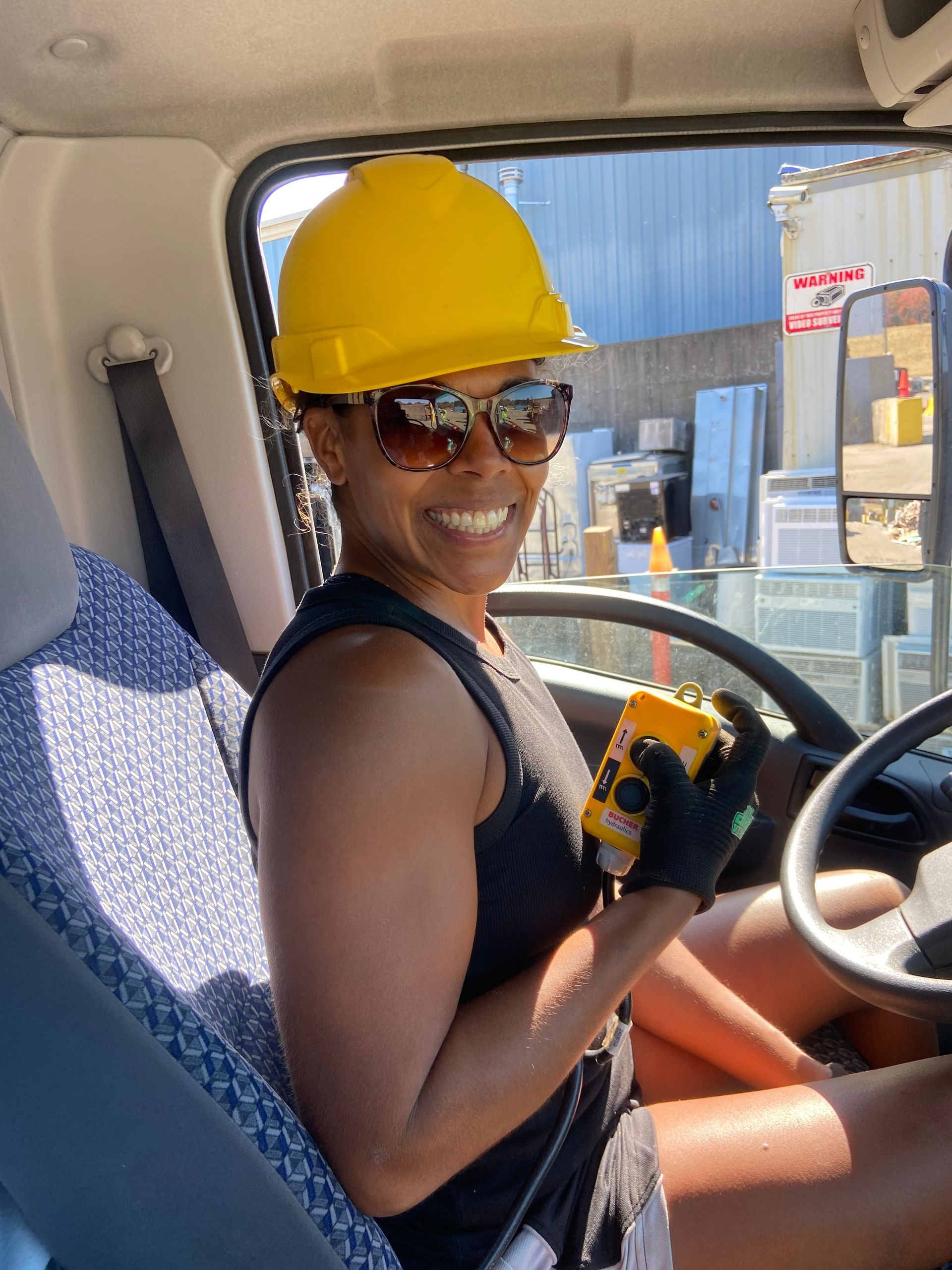 A woman wearing a yellow hard hat and sunglasses is sitting in the driver 's seat of a truck.