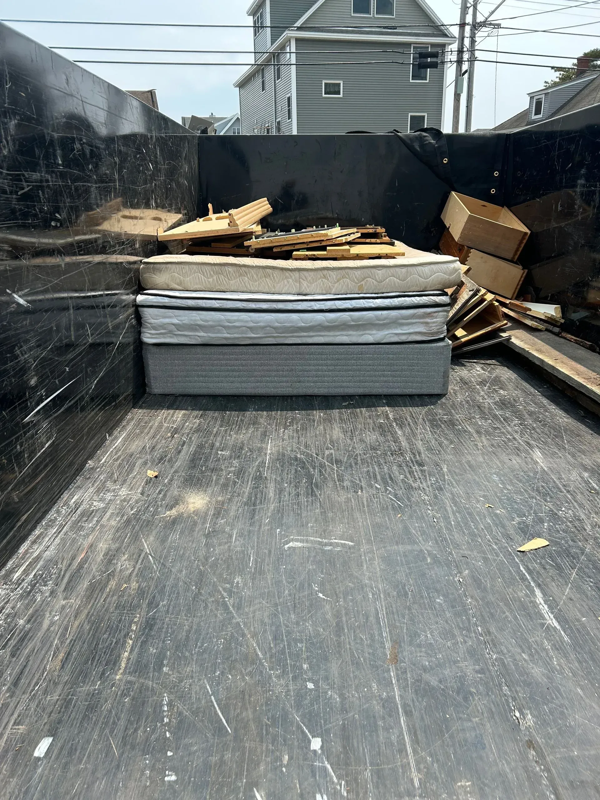 A dumpster filled with wood and boxes with a house in the background.