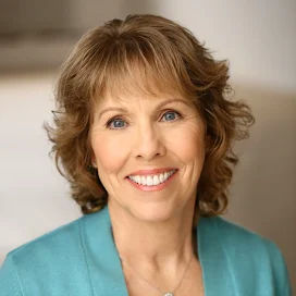 A woman in a blue jacket and necklace is smiling for the camera.
