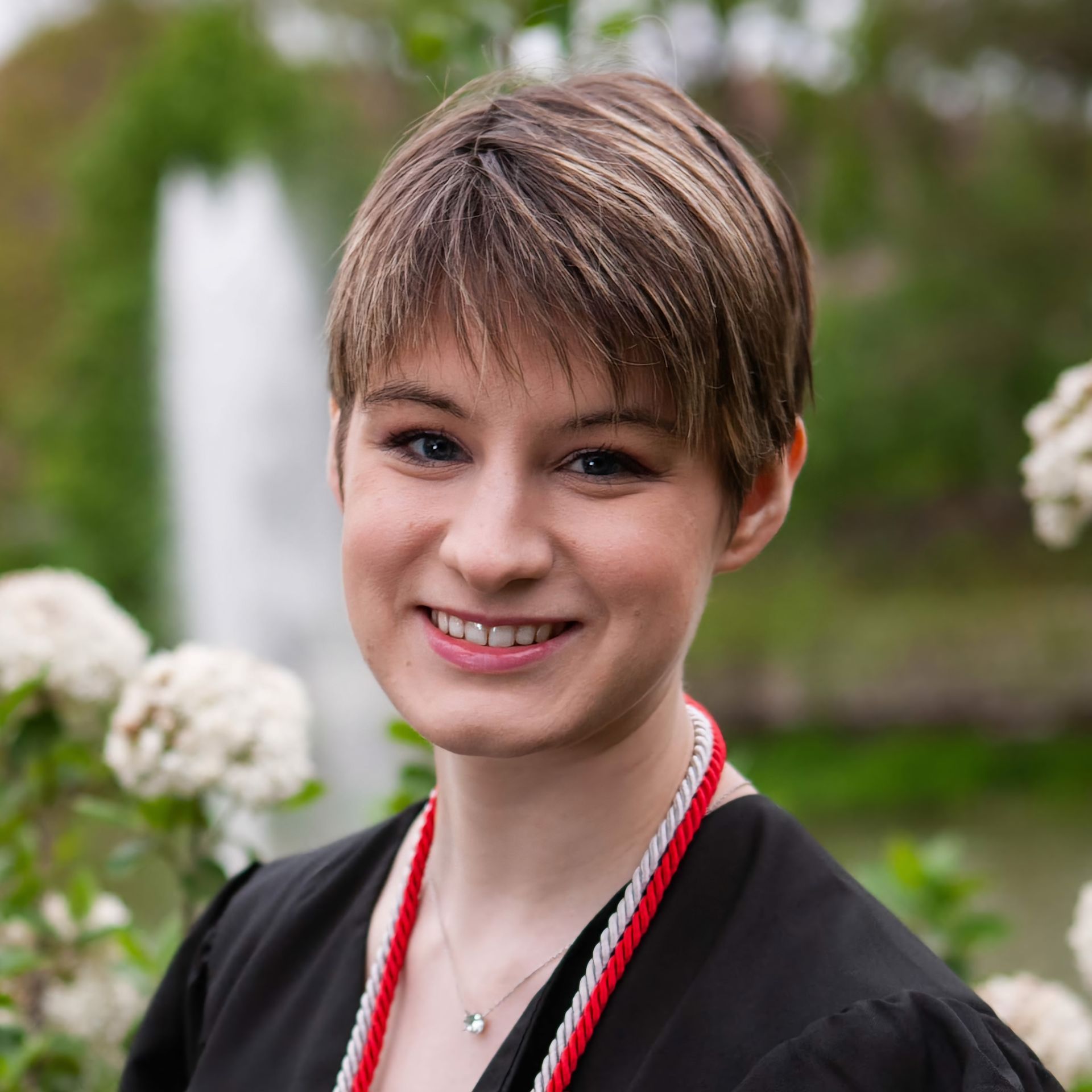 A woman wearing a black shirt and a red necklace smiles for the camera