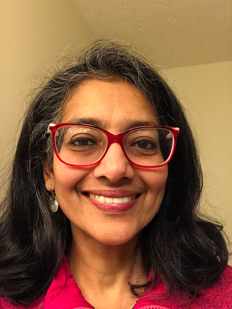 A woman wearing glasses and a pink shirt is smiling for the camera.