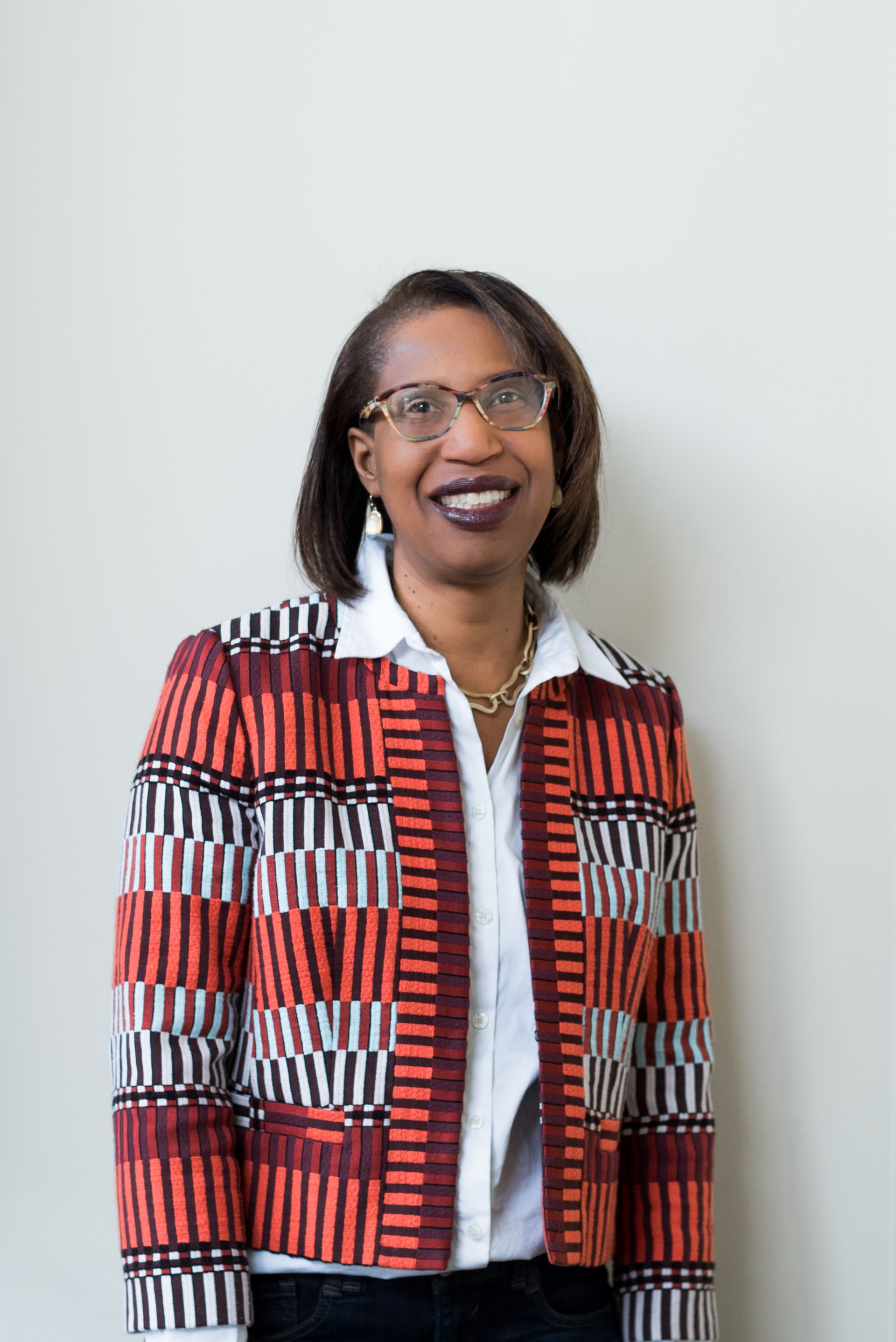 A woman wearing glasses and a colorful jacket is smiling for the camera.