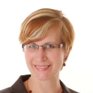 A woman wearing glasses and a necklace smiles for the camera