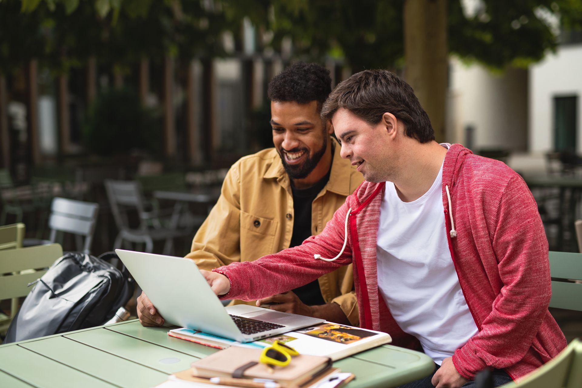 Two men are sitting at a table looking at a laptop computer.