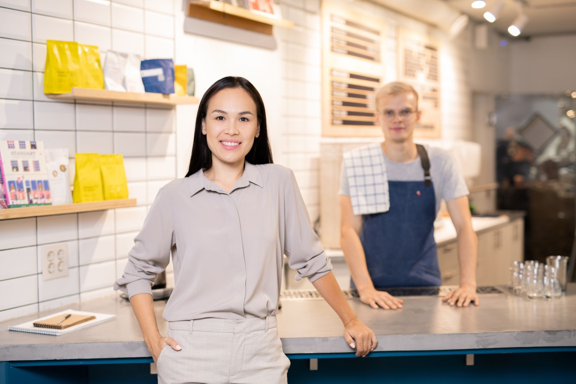 ZBS POS GDC POS smiling Asian woman restaurant owner with white male server in apron behind her at restaurant cafe counter