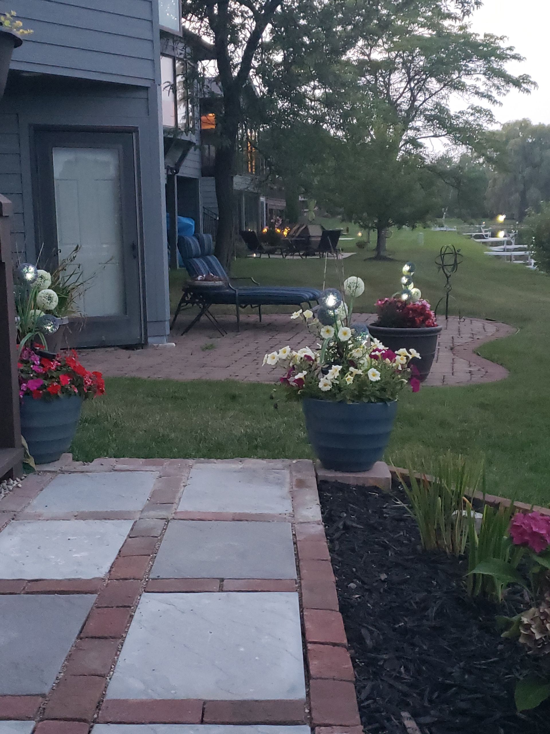 A brick walkway leading to a patio with flowers in pots
