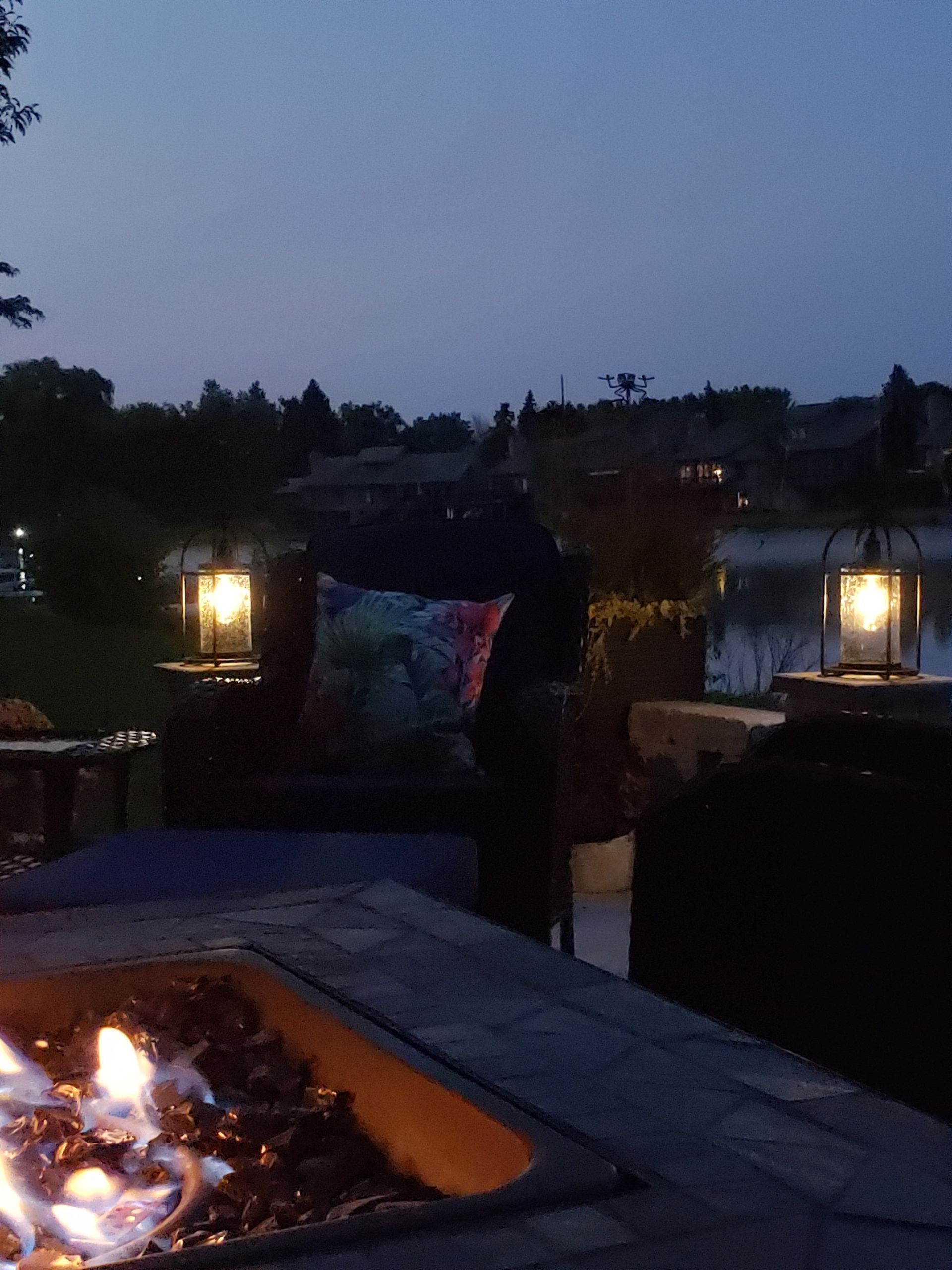 A fire pit is lit up at night with lanterns in the background