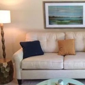 A living room with a couch , lamp , table and painting on the wall.