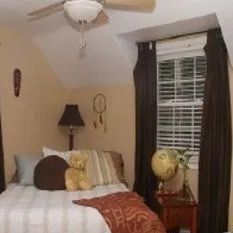 A bedroom with a bed , nightstand , lamp , globe and ceiling fan.