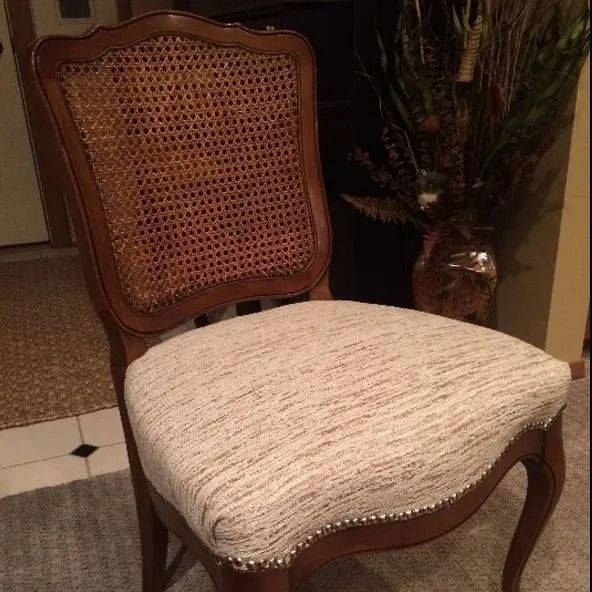 A chair with a wicker back and a white seat is sitting next to a vase of flowers.