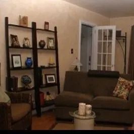 A living room with a couch , chair , coffee table and bookshelf.