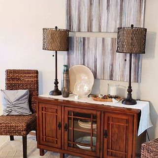 A living room with a wooden cabinet , chairs , lamps and a painting on the wall.
