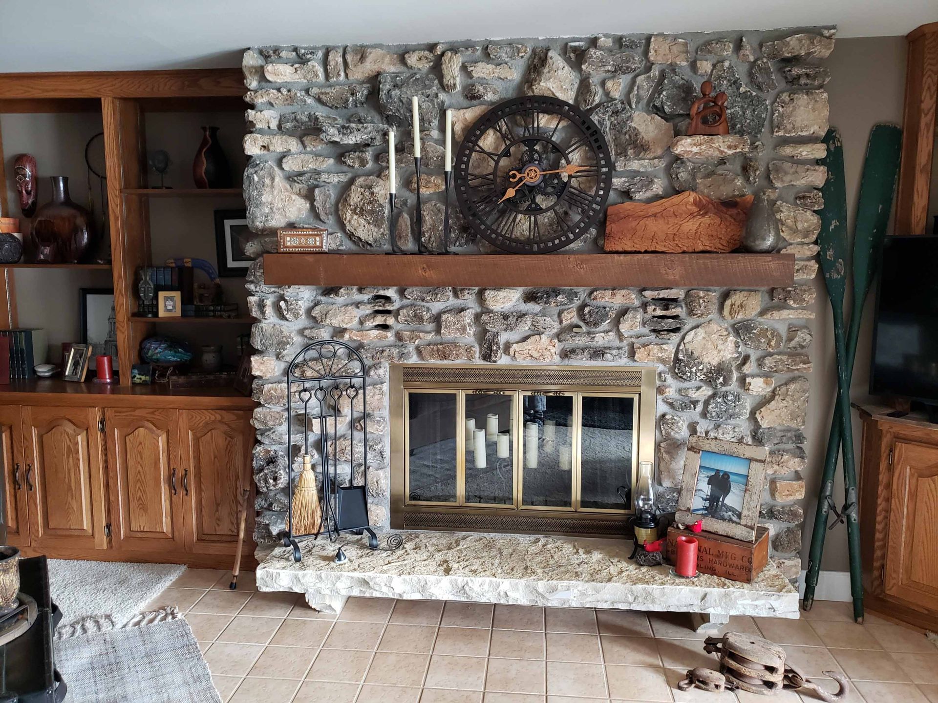 A living room with a stone fireplace and a clock on the mantle.