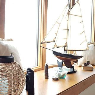 A model sailboat is sitting on a window sill next to binoculars.