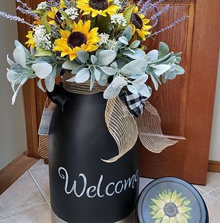 A black vase filled with flowers and the word welcome on it.